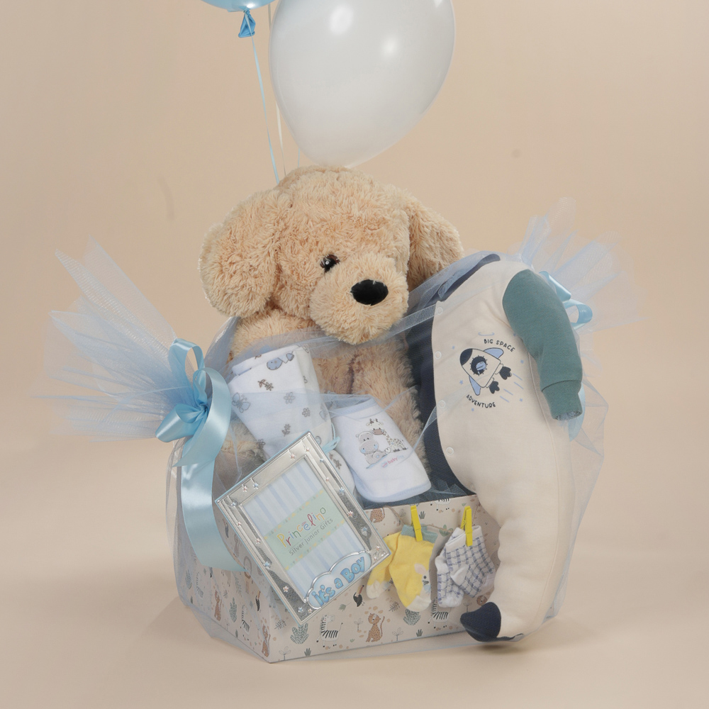 Κοντινή λήψη δώρου γέννησης για αγόρι με λούτρινο σκυλάκι βρεφικά ρούχα, ασημένια κορνίζα "It's a boy" και μπαλόνια σε κουτί Babyline